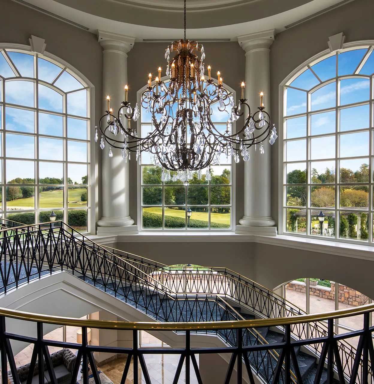 Grand staircase with black and gold railing below large windows and ornate chandelier