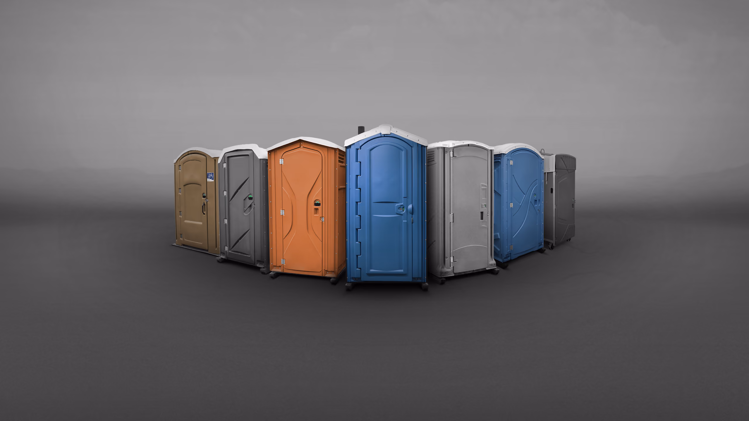 A series of portable toilets in various colors arranged in a circular formation on a gray