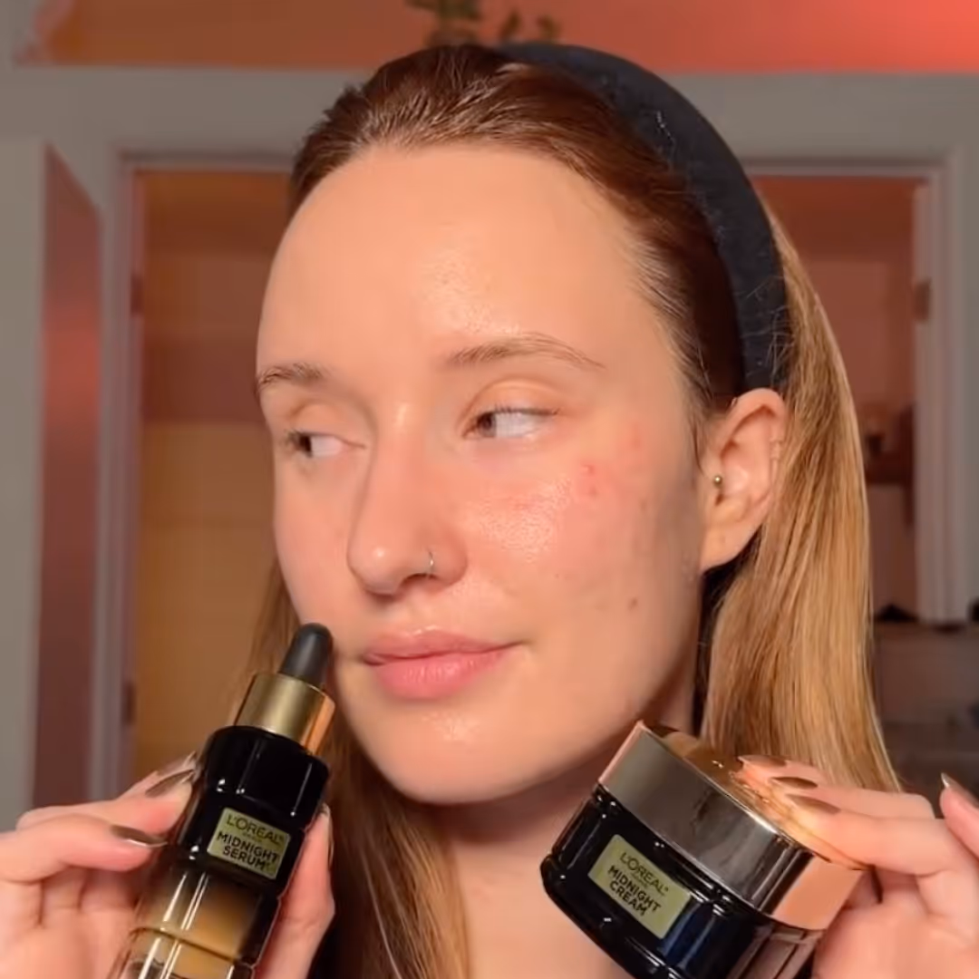 Woman with clear skin holding L'Oreal Midnight Serum and Midnight Cream skincare products.
