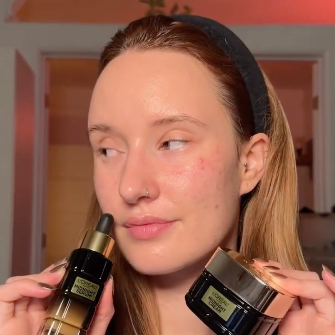 Woman with clear skin holding L'Oreal Midnight Serum and Midnight Cream skincare products.