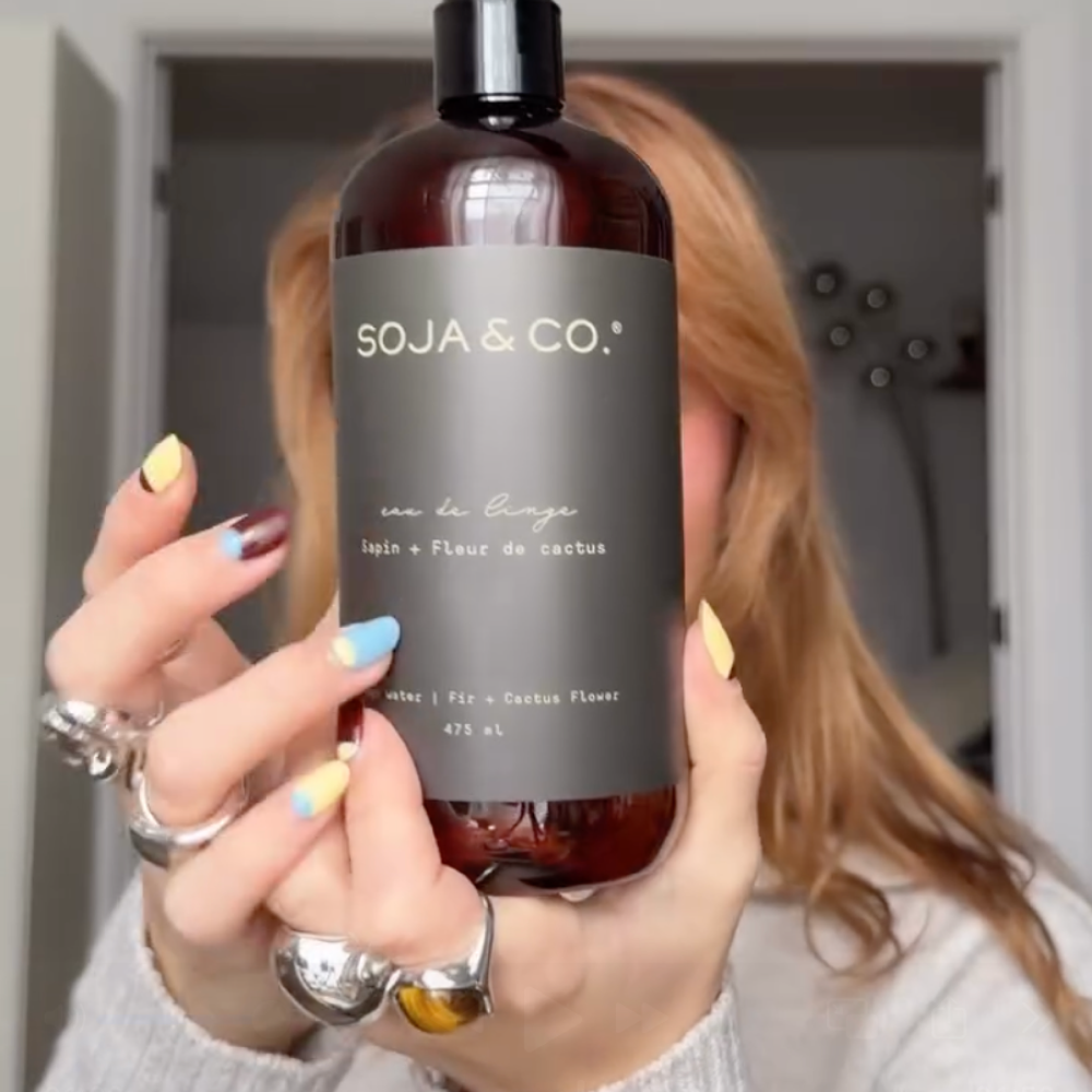 Person holding a brown bottle of SOJA & CO. linen spray with the scent Fir and Cactus Flower, 475 ml.