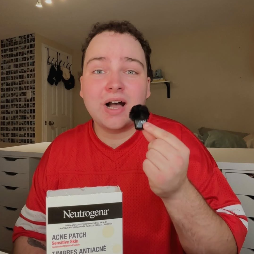 Person in red shirt holding a Neutrogena acne patch box and showing a small black microphone windscreen.