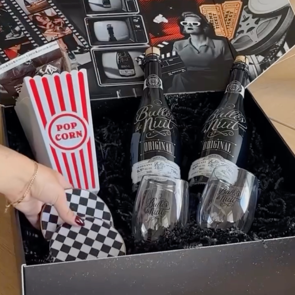 Gift box containing two bottles of Bulles de Nuit Original sparkling wine, two branded glasses, a popcorn container, and checkered coasters.