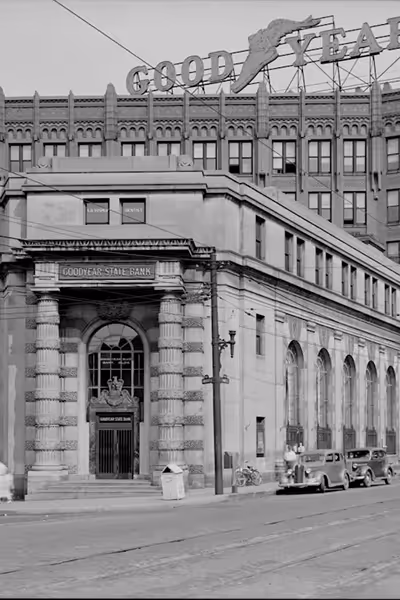 Historic Goodyear State Bank building with vintage cars parked on the street and a Goodyear sign on top of the adjacent building.