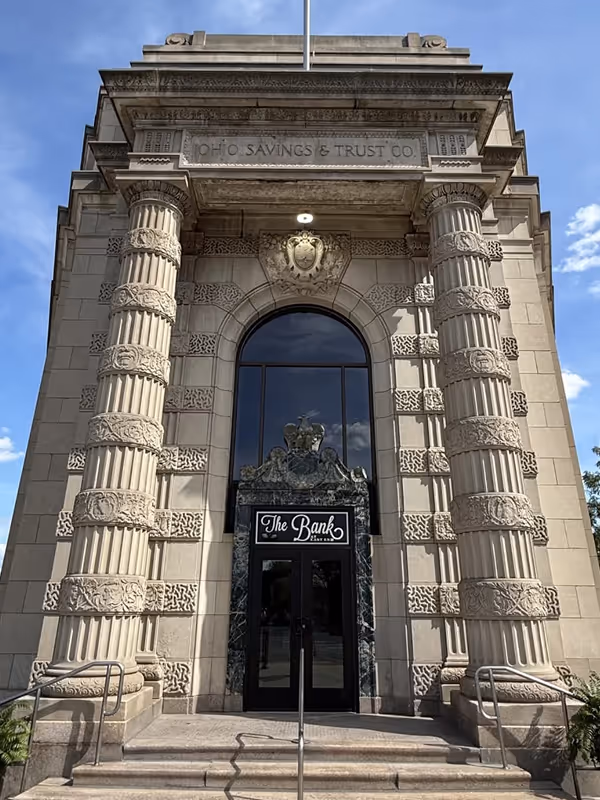 Front entrance of Ohio Savings & Trust Co. building with tall ornate columns and a black door labeled 'The Bank'.
