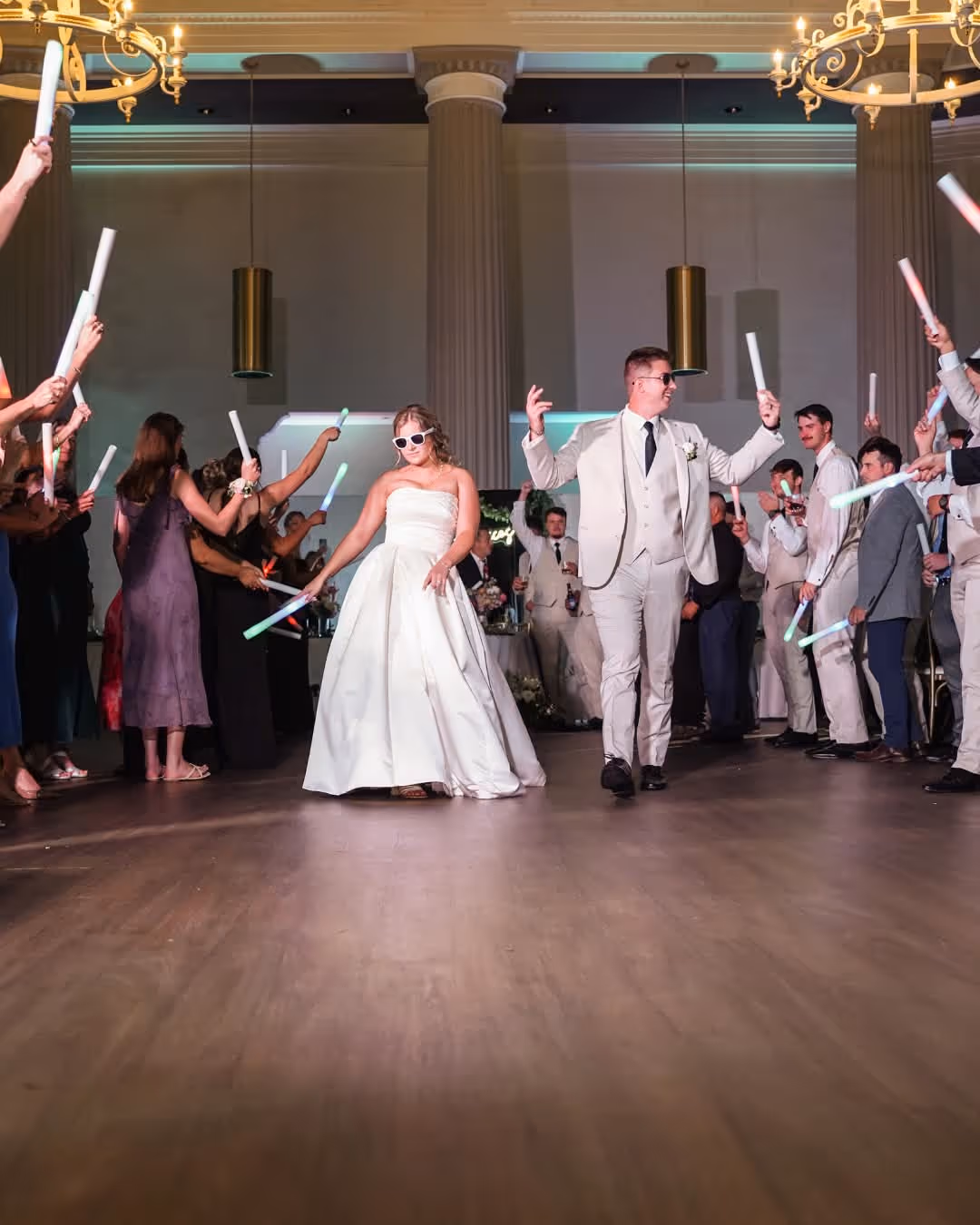 Bride and groom dancing in the center of a wedding reception while guests wave glowing light sticks around them.