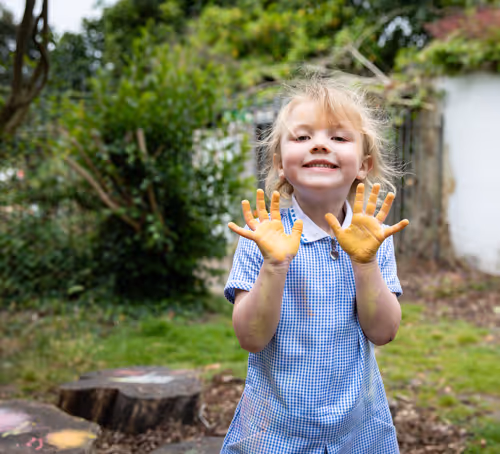 A young student holding up their hands with paint on.