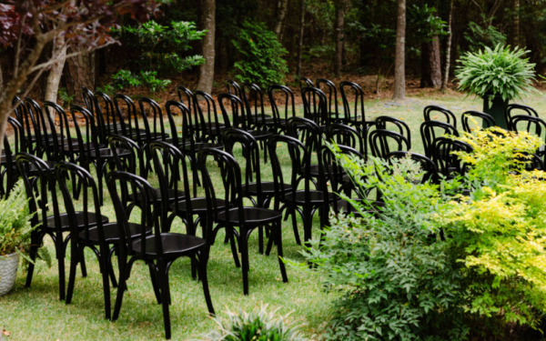 Outdoor wedding ceremony seating with black chairs arranged on a garden lawn surrounded by lush greenery in the Outer Banks.