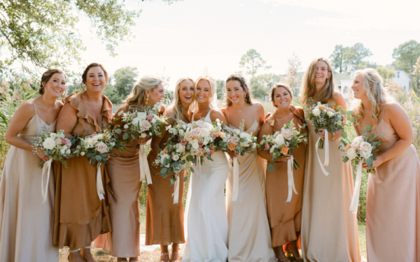 Bride with bridesmaids in pink and copper dresses holding bouquets by Flower Girls OBX