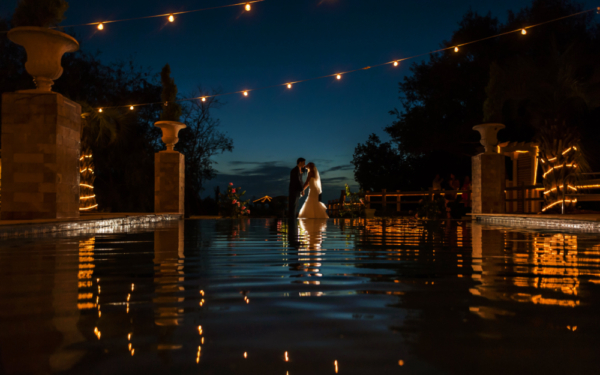 Bride and Groom standing by pool at sunset 