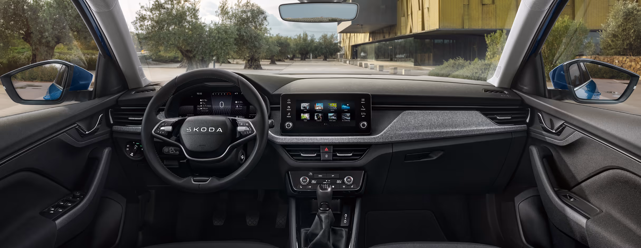 Gesamtansicht des Cockpits im Škoda Kamiq Balance mit Fokus auf das Armaturenbrett mit grauer Stoff-Dekorleiste. Das Bild zeigt das 2-Speichen-Multifunktionslenkrad vor dem digitalen Kombiinstrument sowie das zentral angeordnete Infotainment-Display. Drei grüne Plus-Symbole heben interaktive Bereiche hervor.