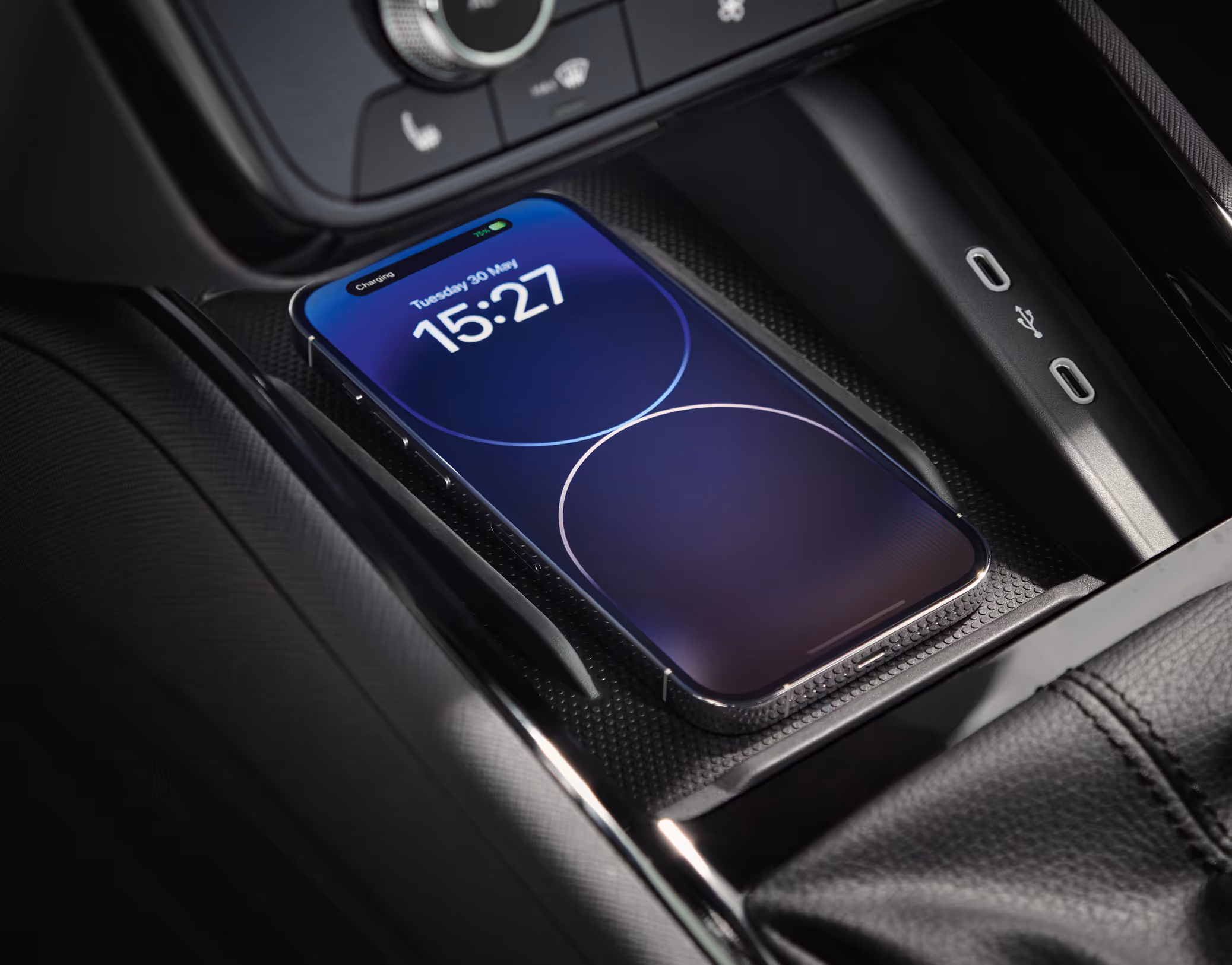 Eine Nahaufnahme zeigt die Phonebox in der Mittelkonsole eines Škoda Kamiq Balance, in der ein Smartphone kabellos geladen wird. Auf dem Bildschirm des Telefons wird der Ladevorgang angezeigt. Neben der Ladeschale sind zwei USB-C-Anschlüsse zu sehen. Darüber das Bedienfeld der Klimaanlage.