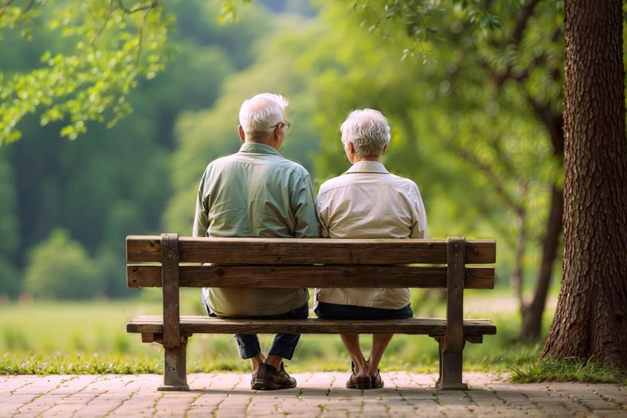 Elderly couple sitting side by side on a wooden bench in a green park.