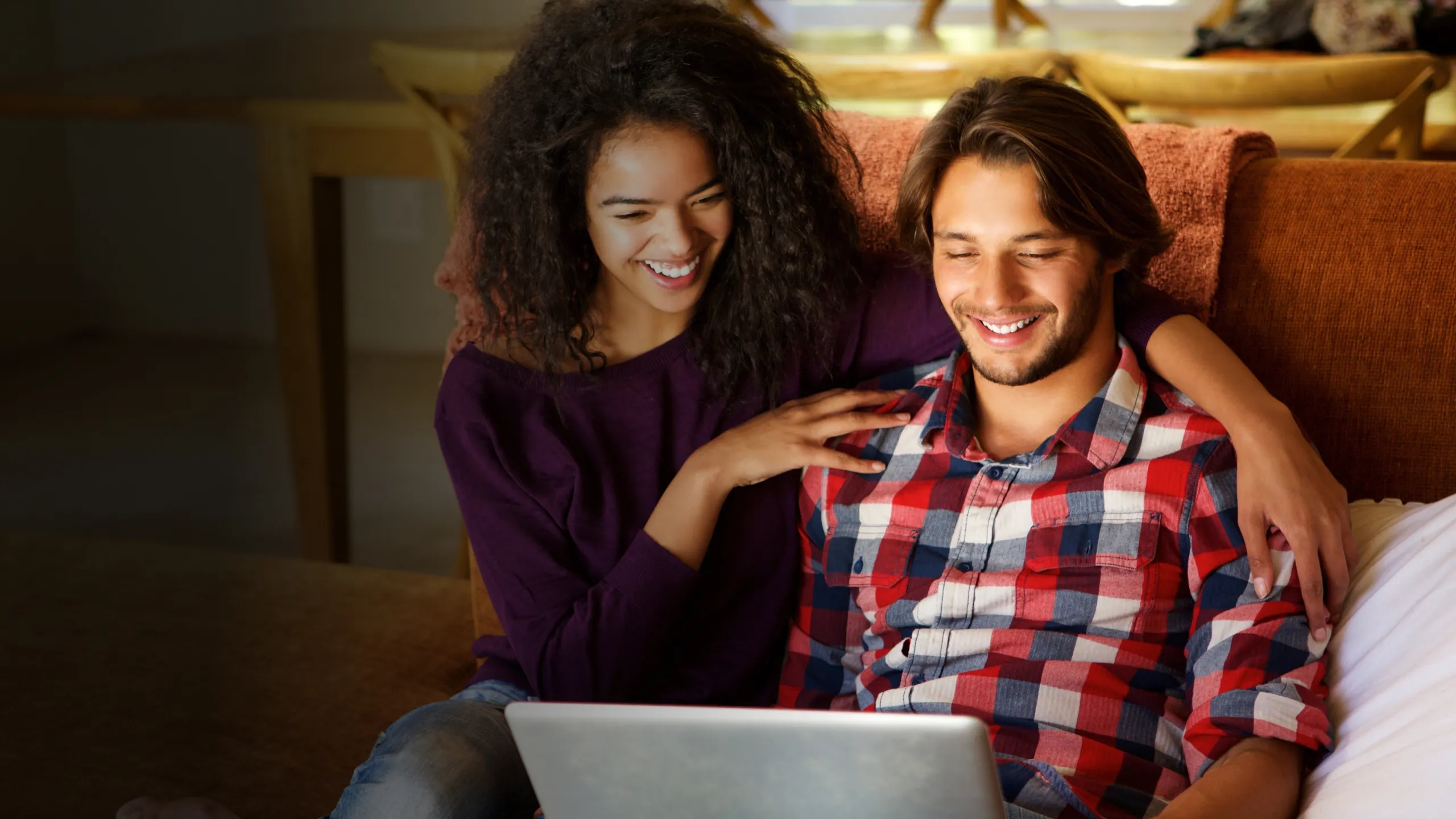 Smiling couple sitting on a couch looking at a laptop together.