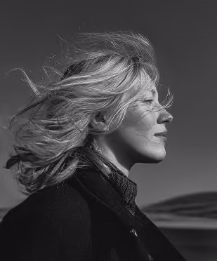Profile of a woman with windblown hair against a dark sky backdrop.