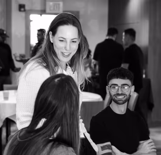 A smiling woman engaging in conversation with two seated people in a social gathering setting.