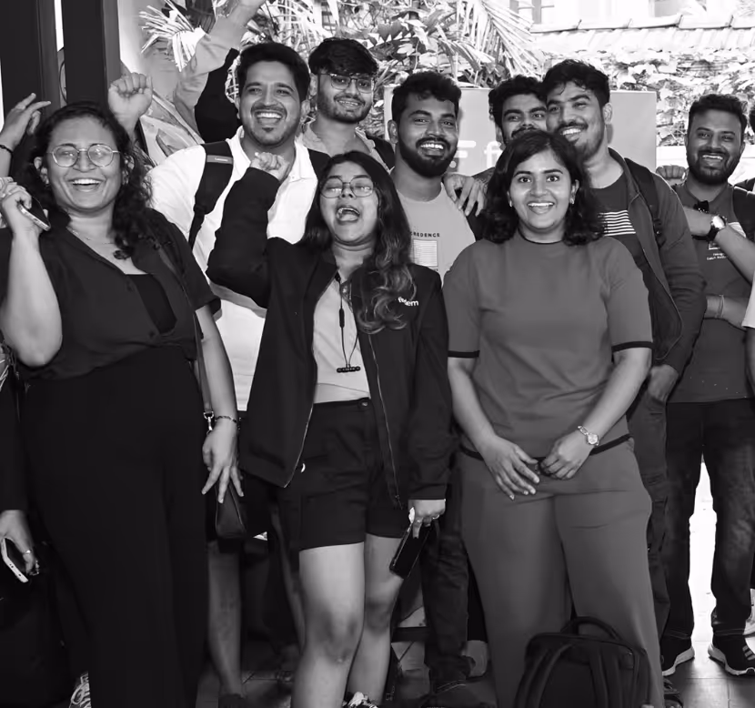 Group of smiling young adults posing indoors, some raising their fists in celebration.