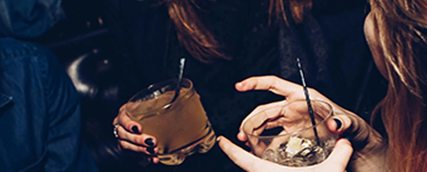 Two people holding glasses with mixed drinks and ice in a dark nightlife setting.