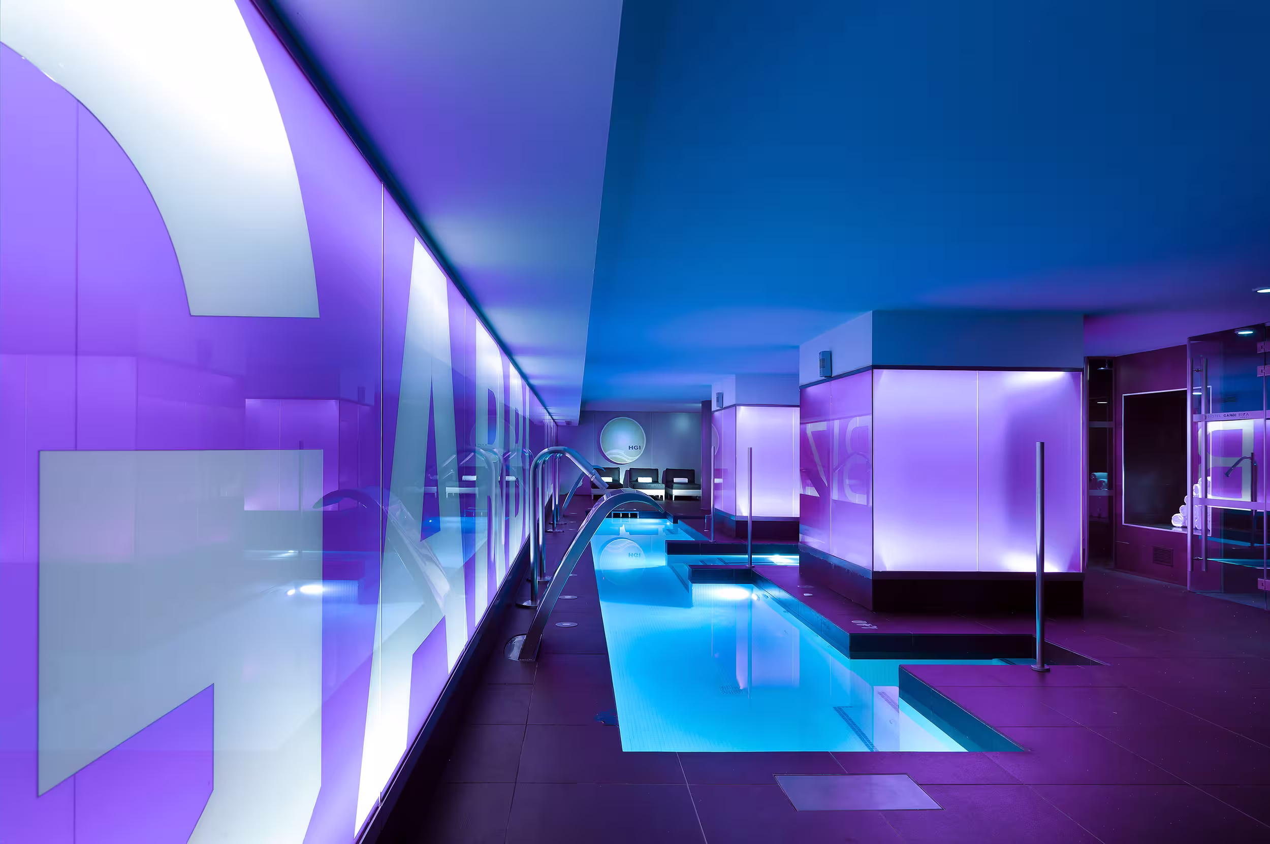 Modern indoor pool area with blue water and purple ambient lighting along the walls and ceiling.