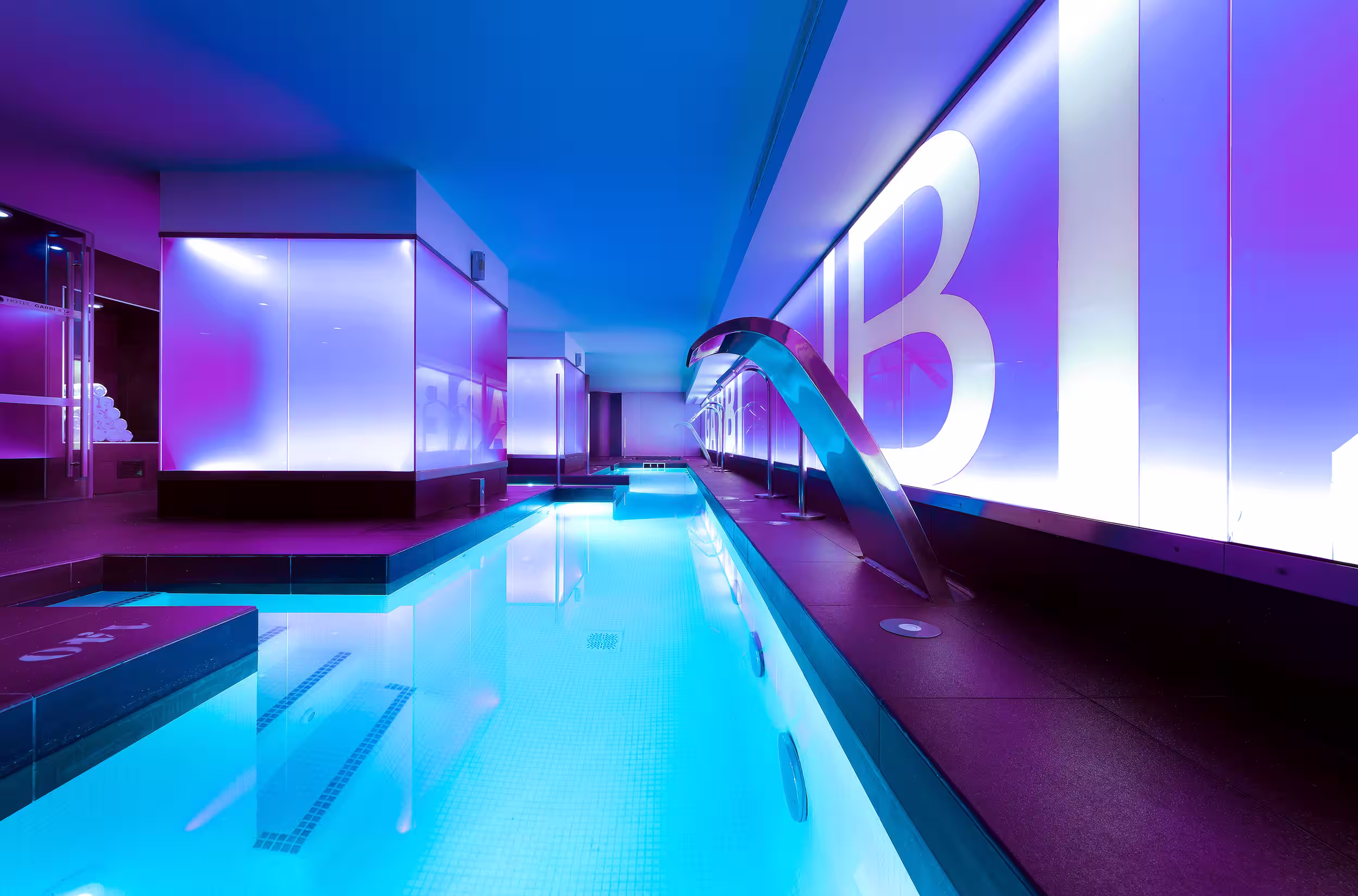 Modern indoor pool with blue water and purple-lit walls featuring large white letters.