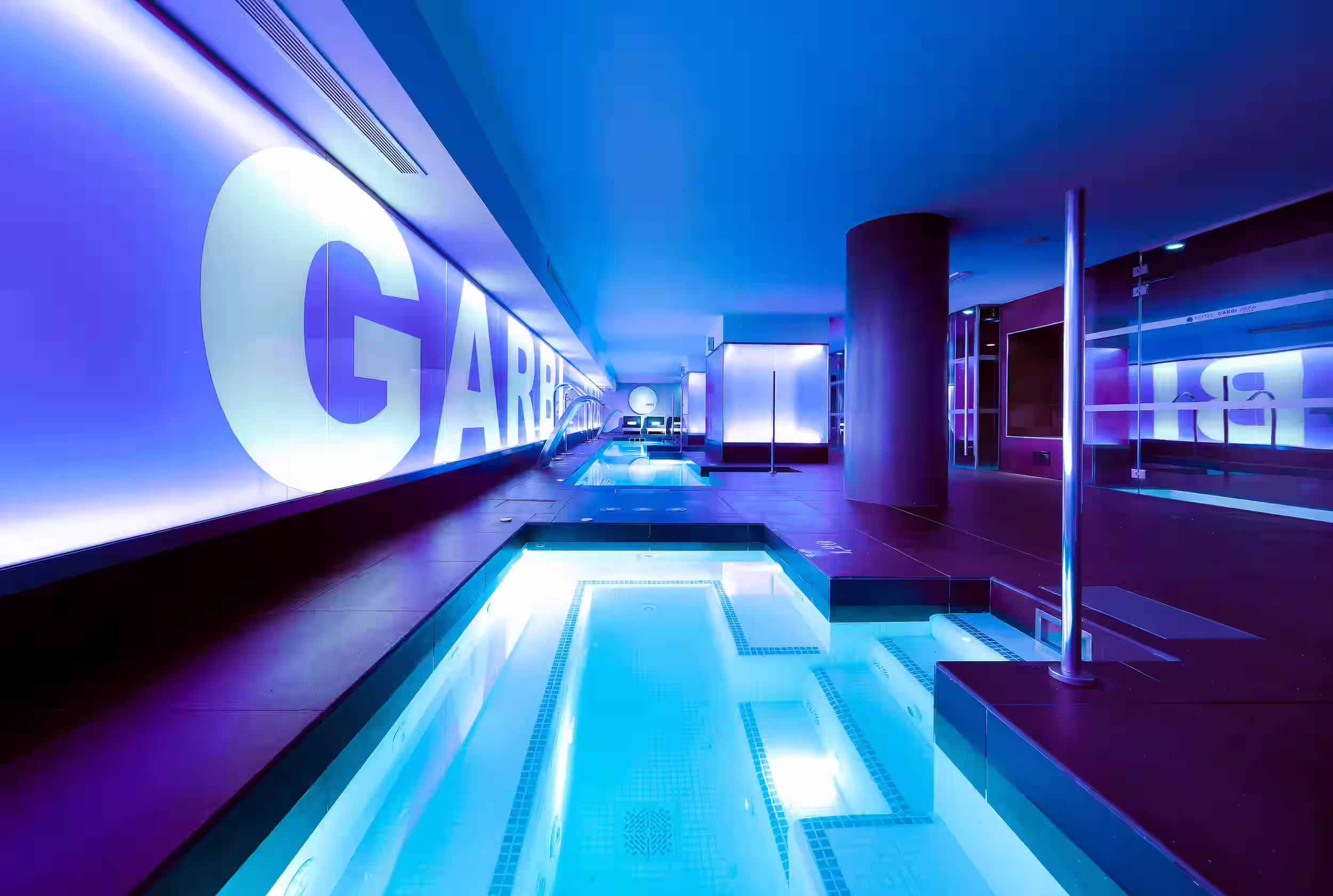 Modern indoor pool with blue water and purple-lit walls featuring large white letters.