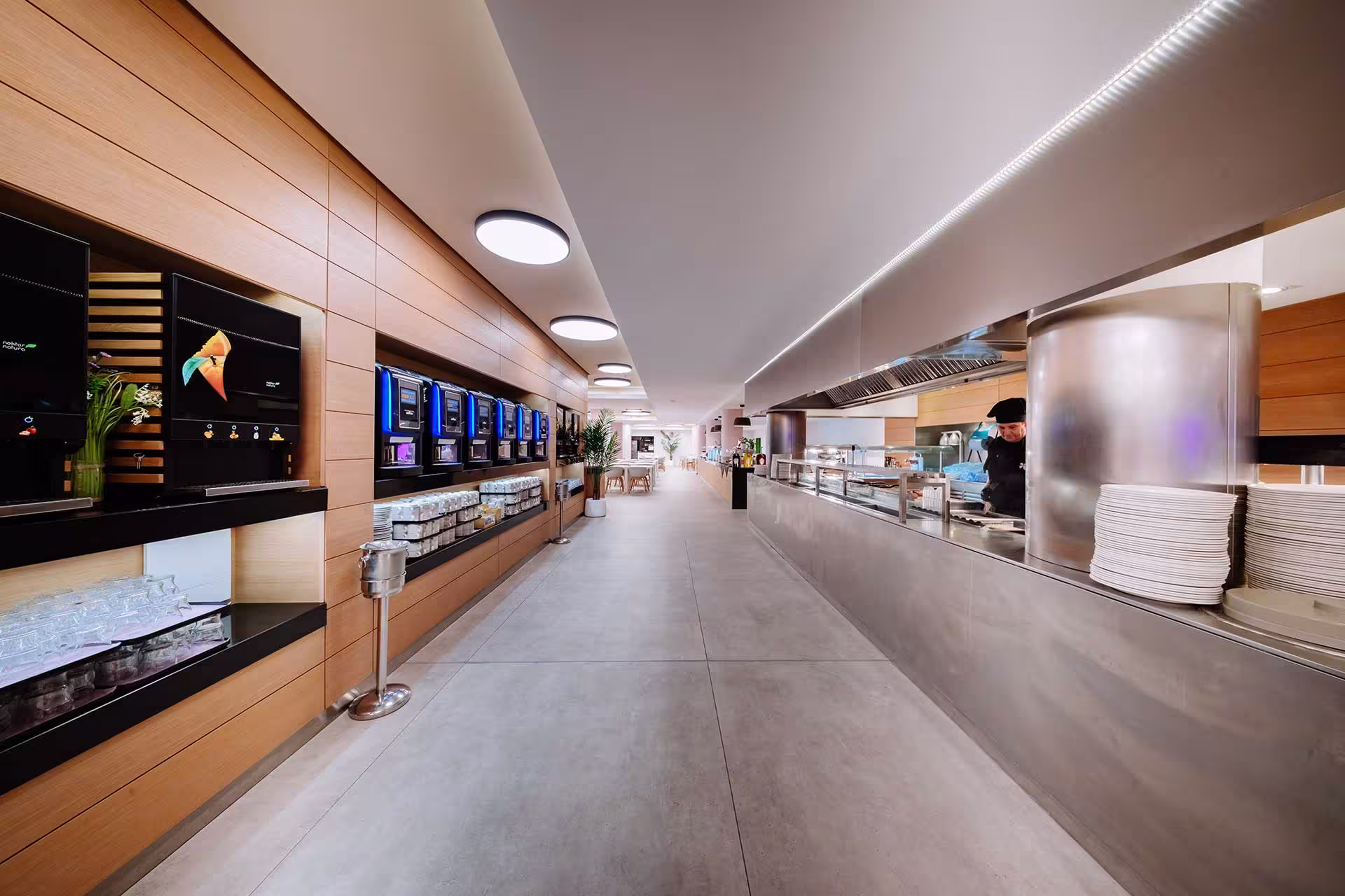 Modern hotel buffet area with coffee machines, food service counter, and a chef.