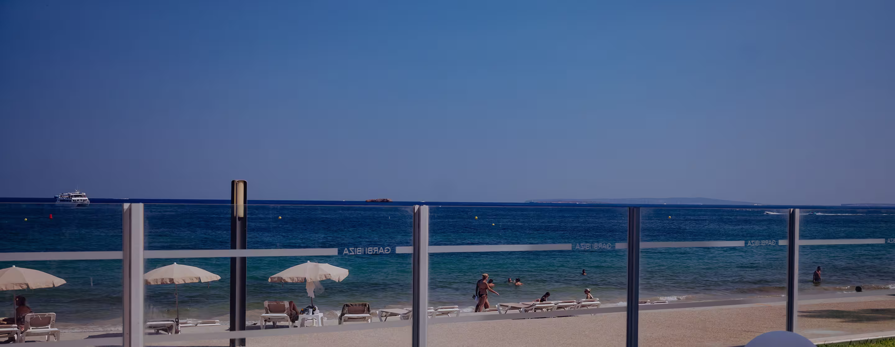 Beach scene with people lounging on chairs under umbrellas and swimming in the sea on a sunny day.