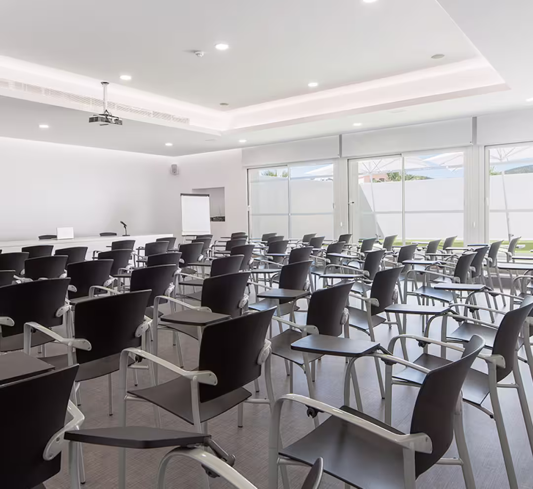 Empty modern conference room with rows of black chairs equipped with writing desks, a whiteboard, and a ceiling projector.