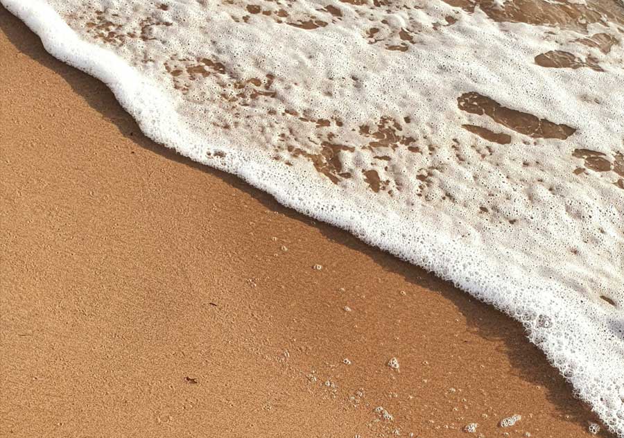 Foamy ocean wave gently washing over smooth sandy beach.