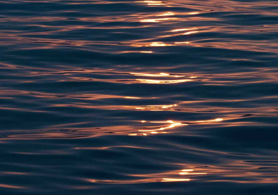 Reflection of warm sunlight on gentle dark ocean waves at sunset.