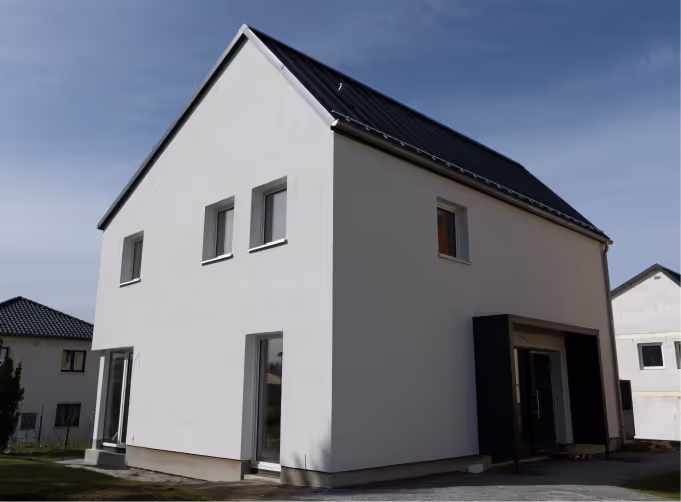 Modernes, zweistöckiges weißes Wohnhaus mit Satteldach und großen Fenstern unter bewölktem Himmel.