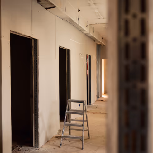 Innenflur einer Baustelle mit unvollständigen Wänden und einer Leiter in der Mitte.