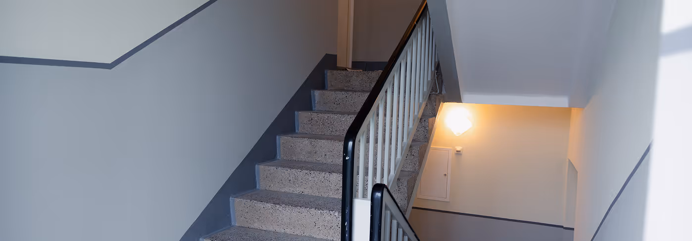 Innenansicht eines modernen Treppenhauses mit grauen Stufen, weißen Wänden und einem beleuchteten Wandlicht.