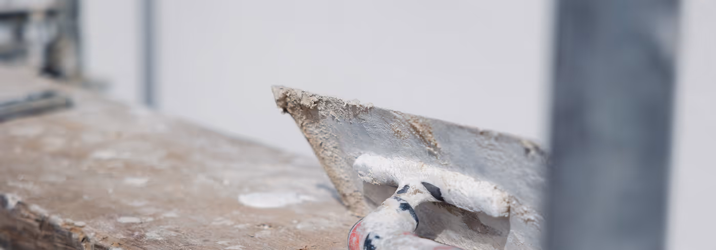 Nahaufnahme eines mit Putz bedeckten Glättekelle-Werkzeugs auf einer verputzten Oberfläche.