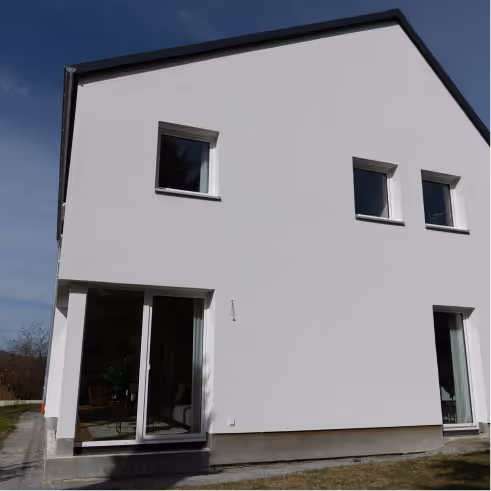 Modernes weißes zweistöckiges Haus mit großen Fenstern und glattem Putz an der Fassade.