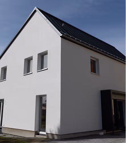 Modernes zweistöckiges Haus mit weißer Fassade und Solarpaneelen auf dem Dach unter blauem Himmel.