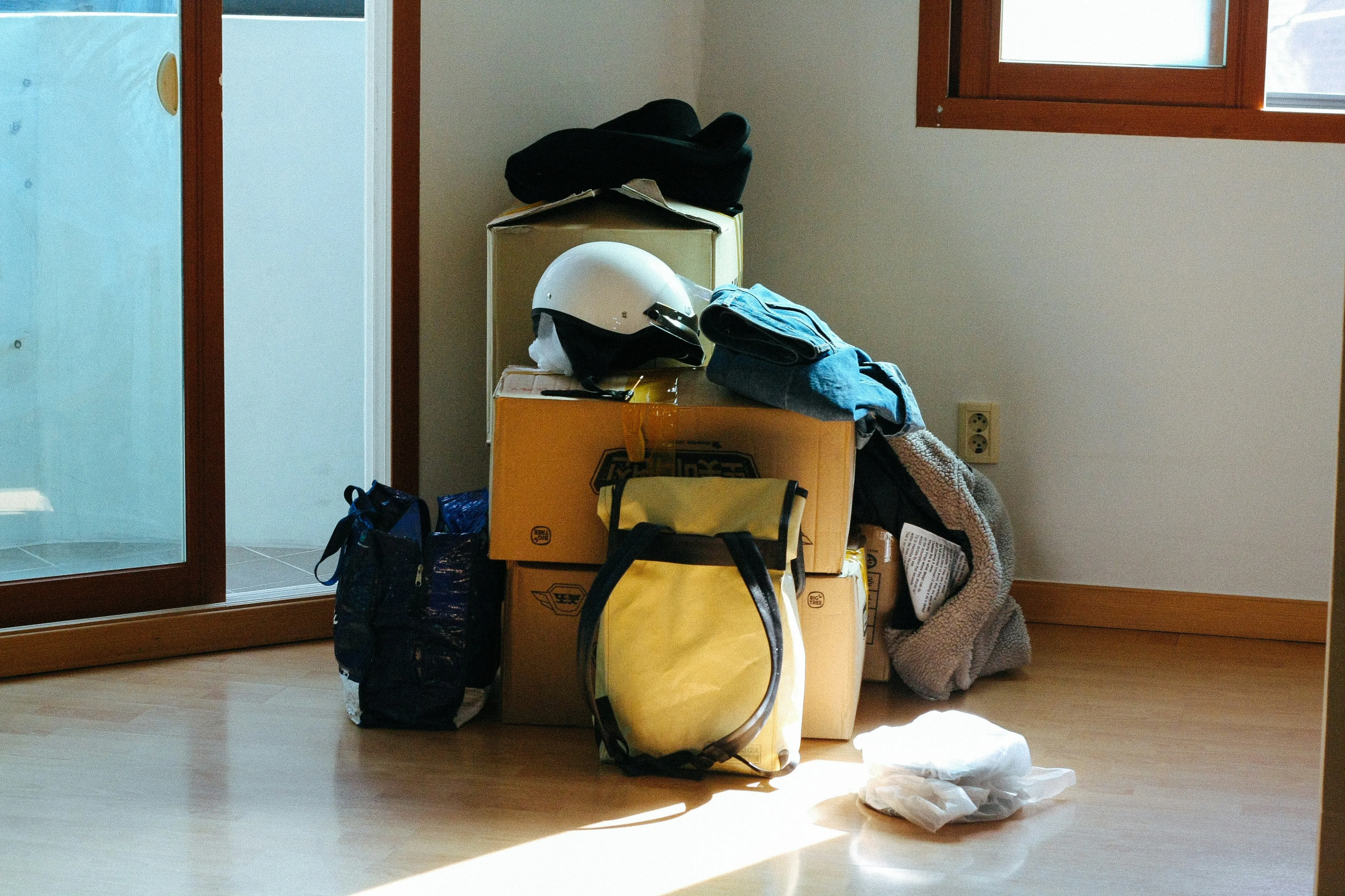 Image of a pile in a home. The pile has cardboard boxes with items like clothing, a helmet, and a backpackoverflowing out of them.