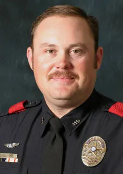 Portrait of a police officer wearing a black uniform with a badge, tie, and red shoulder patches.