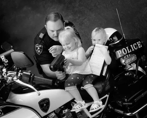 Police officer showing two young children how to hold a police radio while sitting on a police motorcycle.