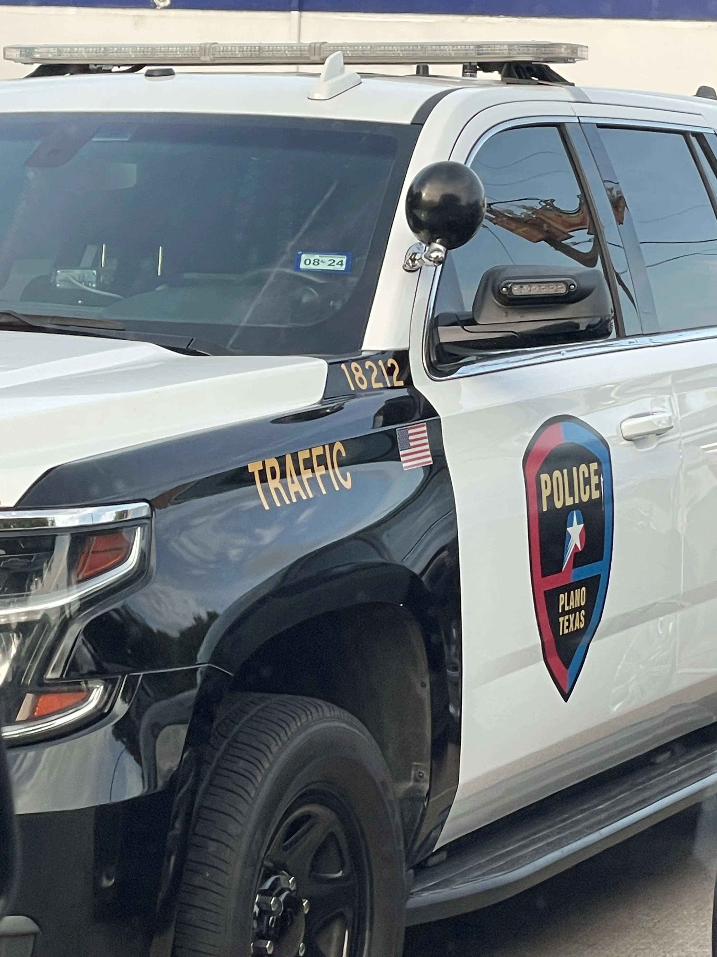 Front side of a black and white Plano, Texas police traffic SUV with a rooftop light bar and an American flag decal.