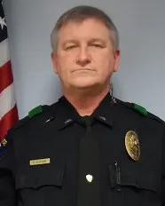 Portrait of a middle-aged police officer in uniform standing in front of a US flag.