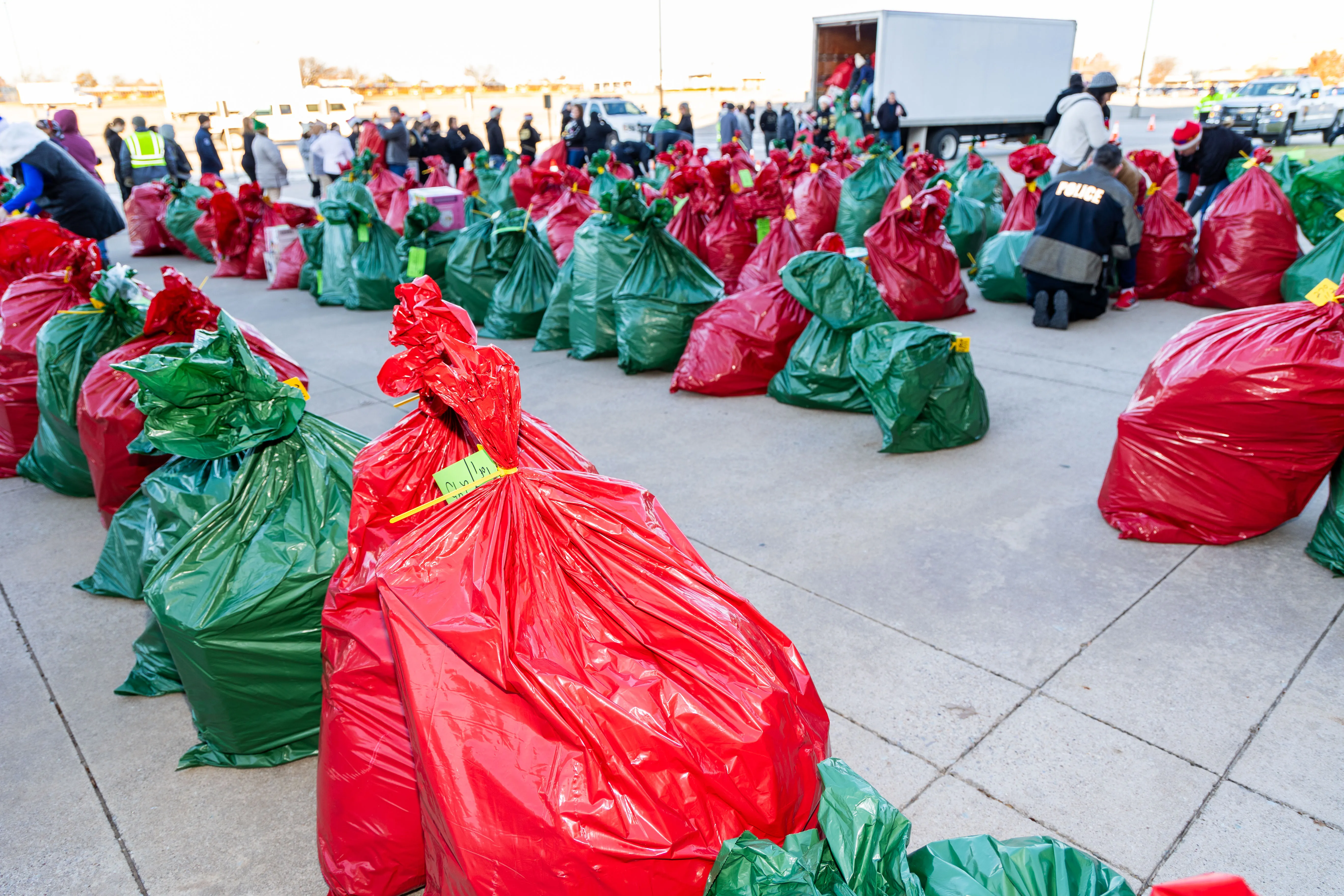 Red and green gift bags lined up outdoors with people unloading a truck and organizing the bags.