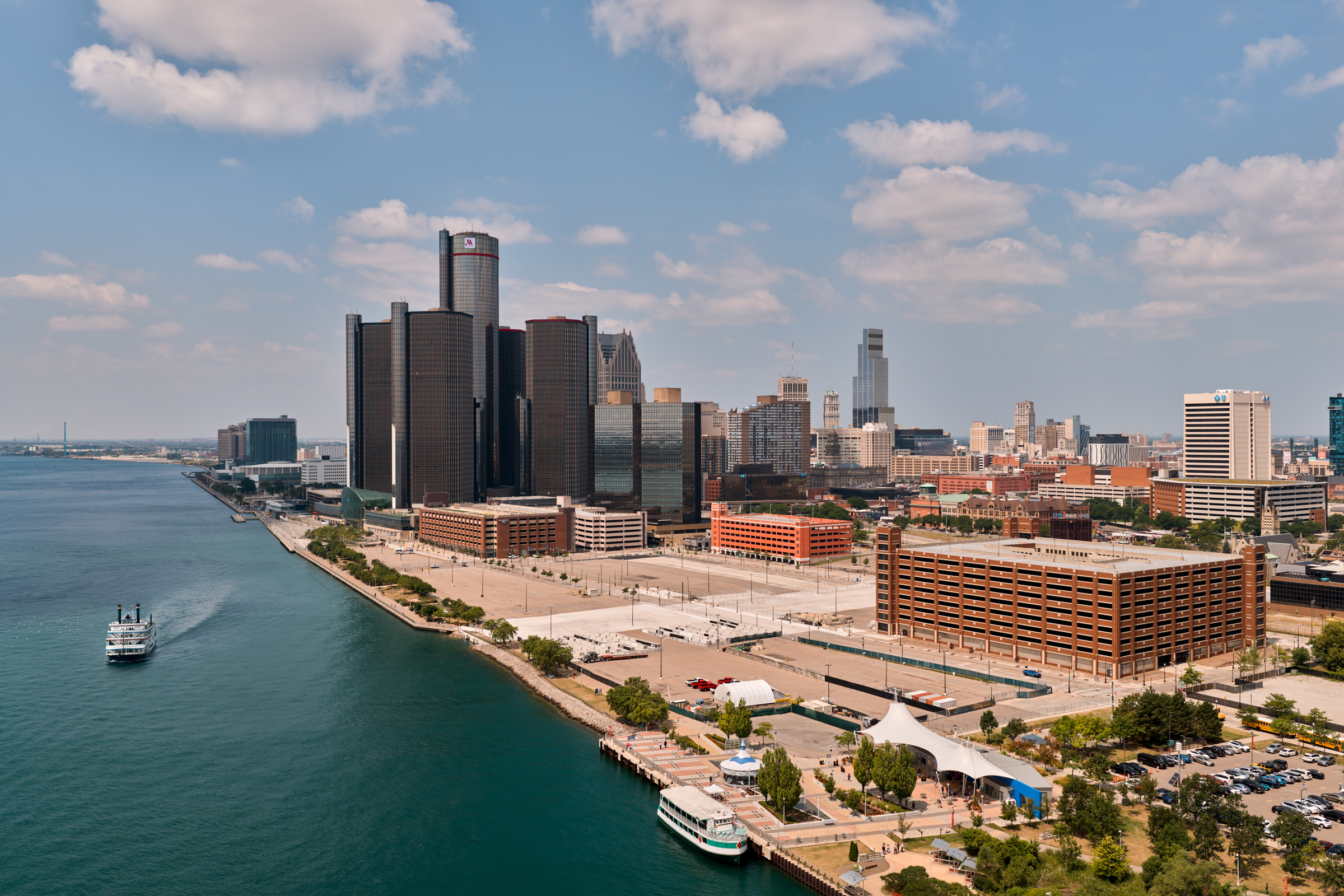 Aerial photo of the undeveloped East Riverfront area, featuring the Renaissance Center in the background and the Detroit River with a ship on the water to picture left.