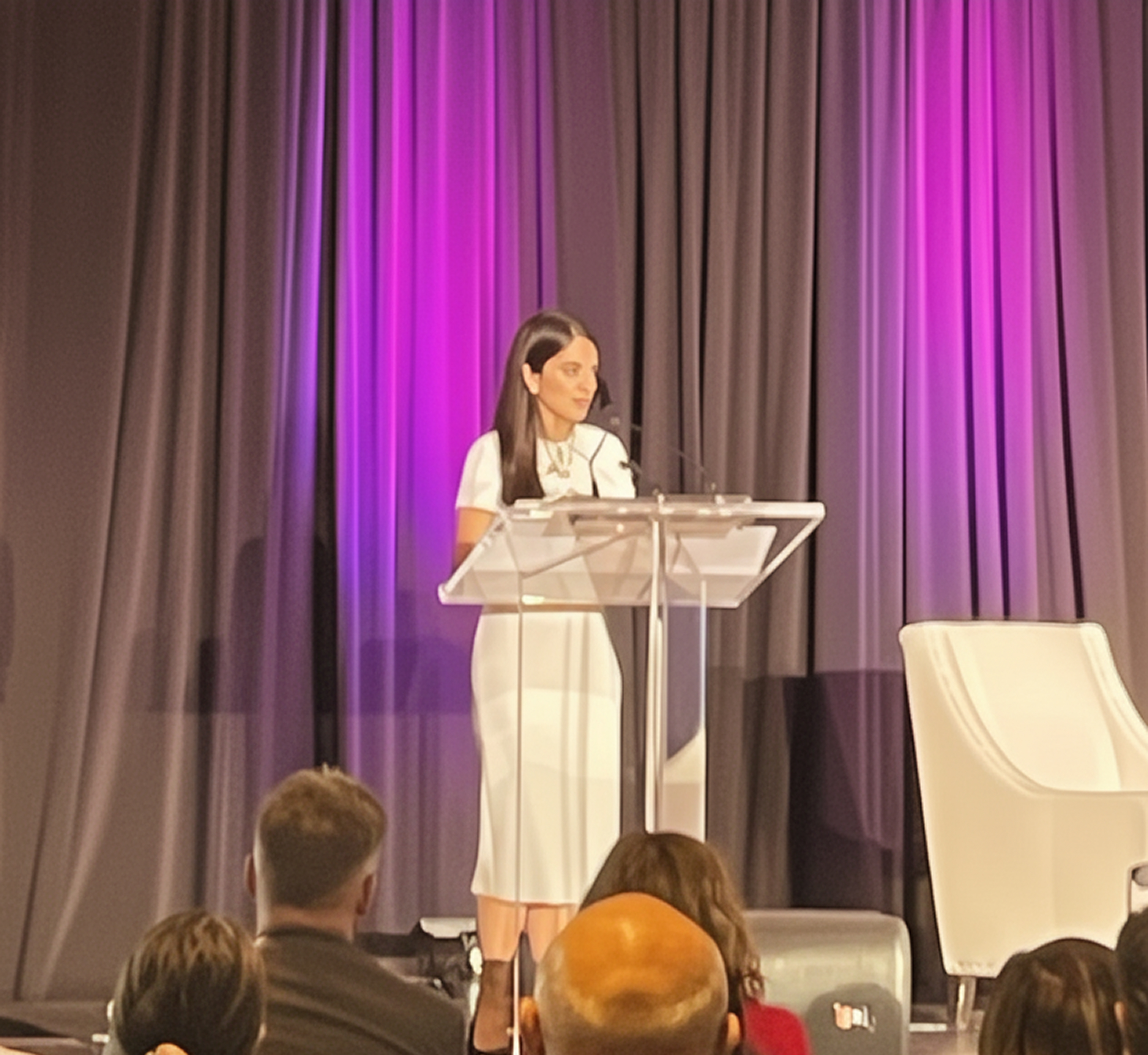 Two men in black coats walk on a sidewalk at night behind a person dressed in a Santa Claus costume.