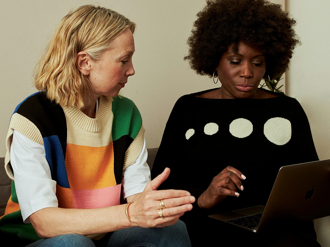 Two women sitting close together, one showing something on a laptop to the other.