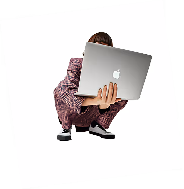 Person crouching while holding an open silver Apple laptop toward the camera.