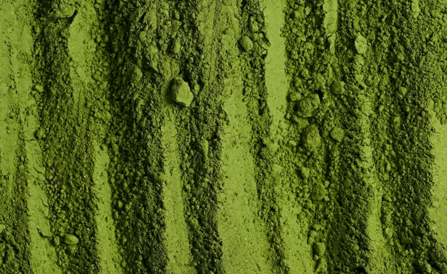 Close-up of fine green matcha powder with varying textures and small clumps.