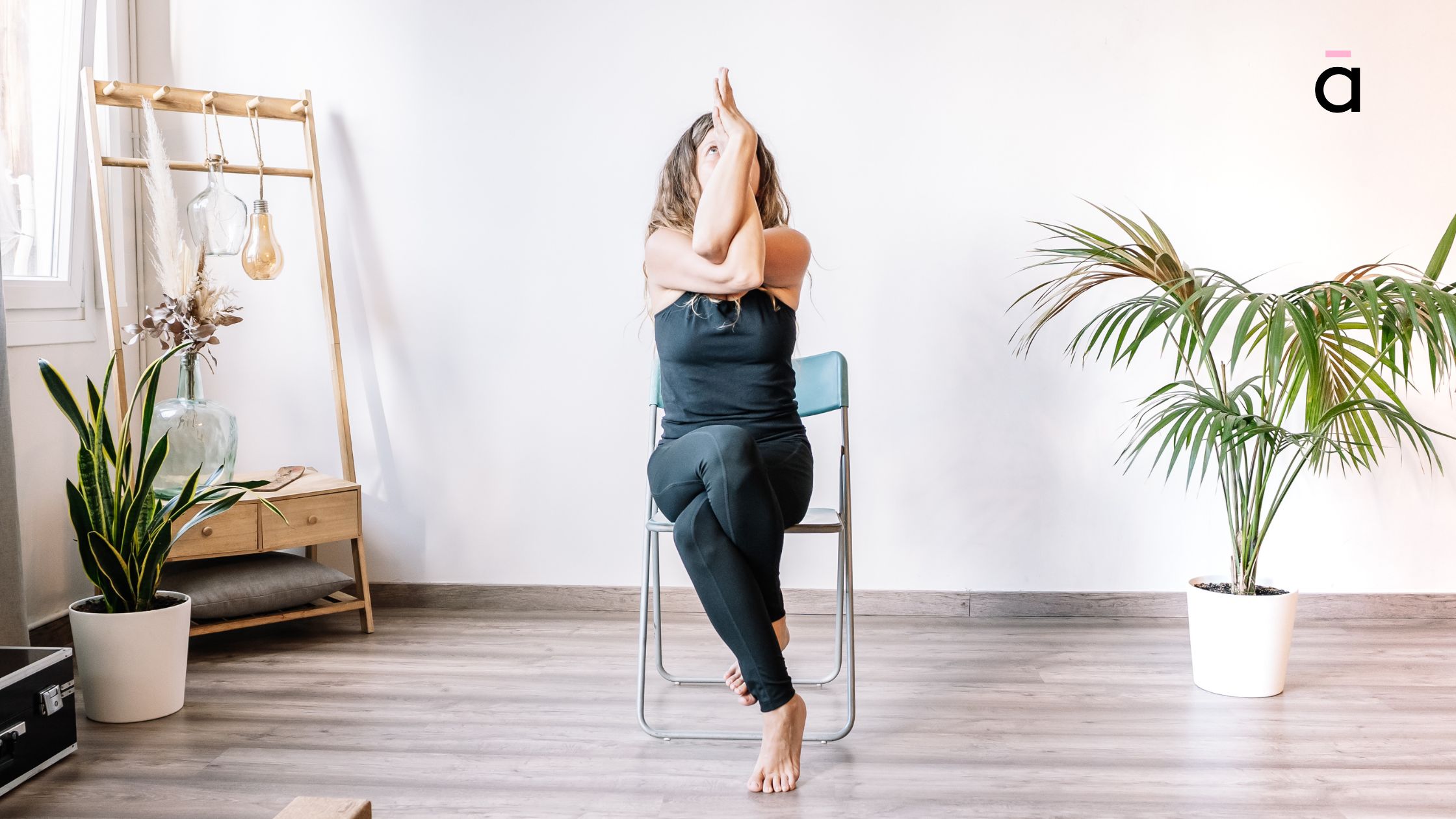 Woman sitting on a chair in Garudasana with arms entwined and focused expression, enhancing mobility and concentration