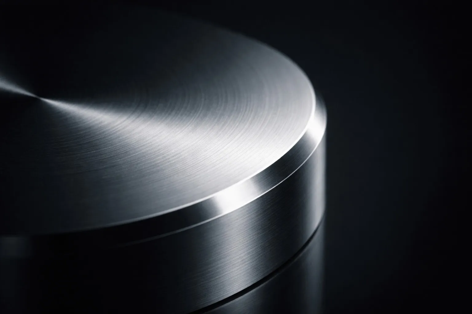 Close-up of a polished metal cylinder with circular brushed texture under studio lighting.