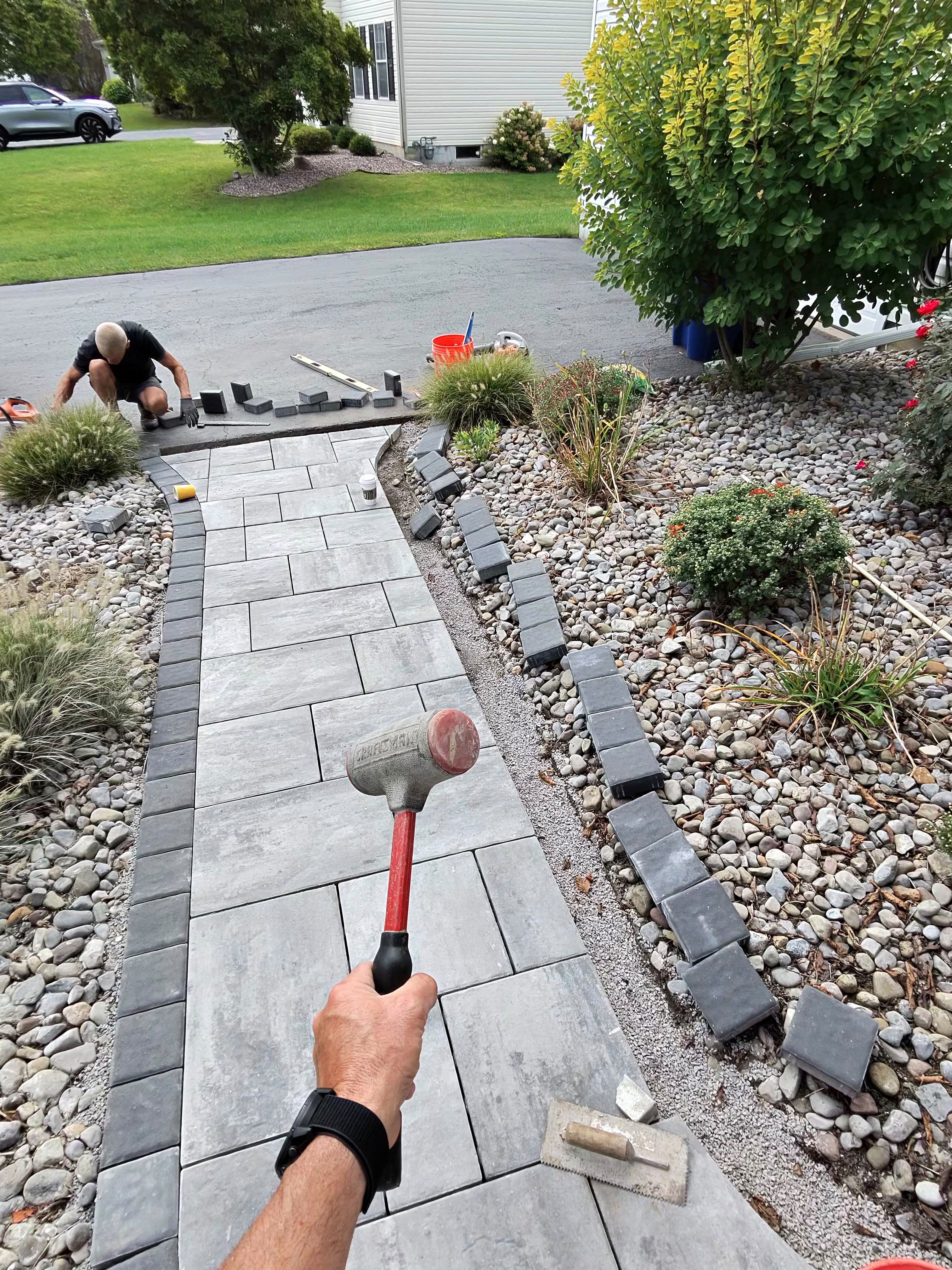 Crew installing a gray paver walkway with charcoal border edging